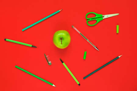 Creative flat lay of school supplies - green pens, pencils, scissors and an apple on a red backgroundの写真素材