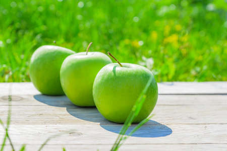 Freshly cropped geen apples on wooden table over grenn grass background.の写真素材