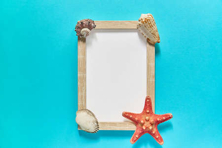 top view of photoframe with seashells and starfish on blue background. Summer vacation concept. Sea...