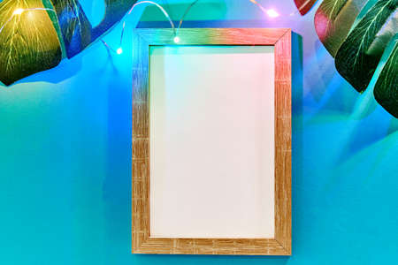 Photo frame and green monstera leaves on blue background with neon lighting. Trendy tropical flat lay concept.の写真素材