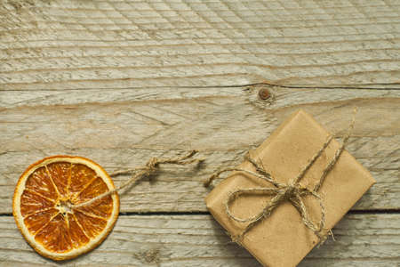 Christmas decor. Dried orange slice and gift box in craft paper on wooden background, top view, minimal flat layの写真素材