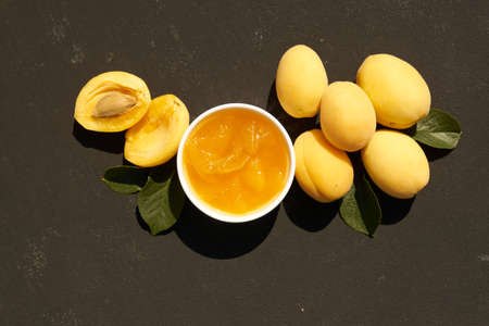 homemade organic apricot jam in white bowl and ripe apricots on black background. Hard light