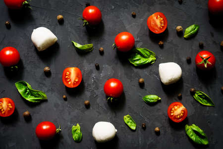 Mozzarella cheese balls with fresh basil leaves and cherry tomatoes, ingredients for Italian Caprese salad, on a black background. Eating patternの写真素材
