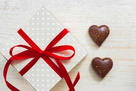 Greeting card for st valentines day. Chocolate sweets in heart shape and giftbox with red celebration ribbon on wooden backgroundの写真素材