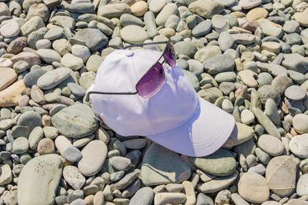 Baseball caps and sunglasses lie on a gravel