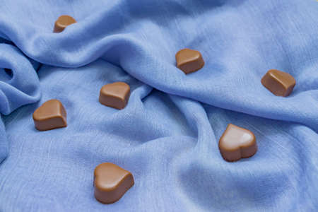 Milk chocolate hearts on blue fabric. St Valentine's holidays background. Love concept