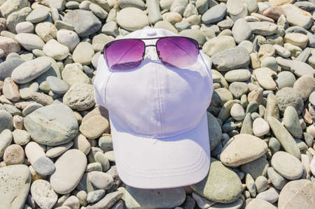 Baseball caps and sunglasses lie on a gravelの写真素材