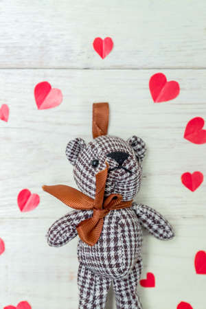Teddy bear among red paper hearts on wooden background. Greeting card with copy space for designの写真素材