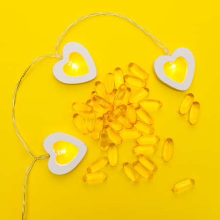omega 3 fish oil gel capsules on yellow background with heart shaped garland with light on. Health...