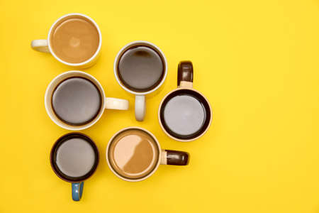 Many cups of different aromatic hot coffee on yellow background, top view, copy space