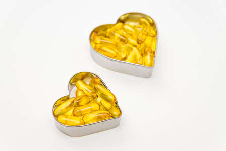 Fish oil capsules in a heart shape boxes on white background, vitamin D supplement, health care conceptの写真素材