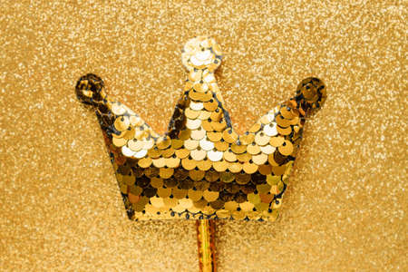 golden magic stick from sequins in crown shape on golden glitter background. Creative flat layclose...