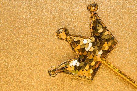 golden magic stick from sequins in crown shape on golden glitter background. Creative flat layclose...