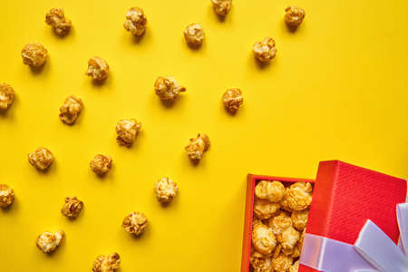 Colorful trendy backdrop with caramel popcorn and red gift box on yellow backgroundの写真素材