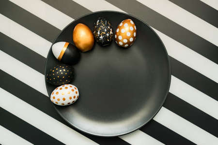 Black and white striped background with white, black and golden decorated eggs on black plate....