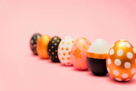 Side view of pink, white, black and golden decorated easter eggs in a row on pink background. Trendy...