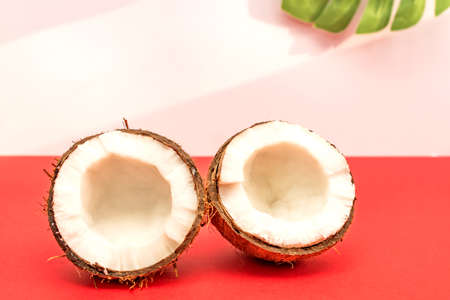 Two halves of fresh raw coconut on red backgound with light shadows in white.