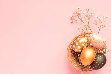 Top view of wooden painted eggs in gold, black and rose colors in wicker basket with branch of...