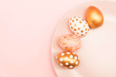 Top view of pink, white and golden decorated eeaster eggs on pink plate on pink background. Trendy...