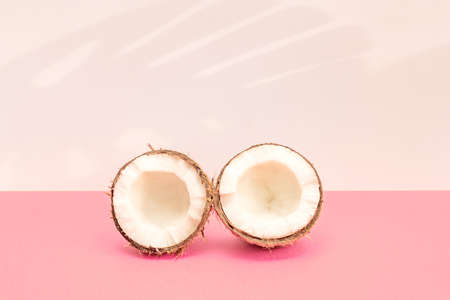 Two halves of fresh raw coconut on pink backgound with kight shadows in white.