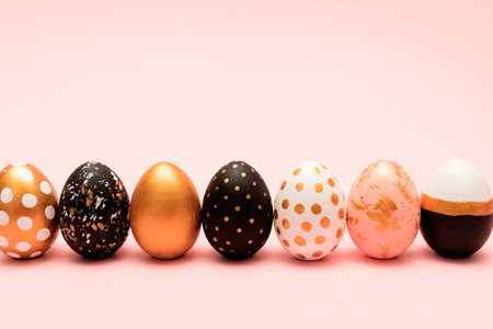 Side view of pink, white, black and golden decorated easter eggs in a row on pink background. Trendy...