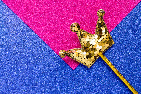 golden magic stick from sequins in crown shape on blue and pink glitter background. Creative flat lay close upの写真素材