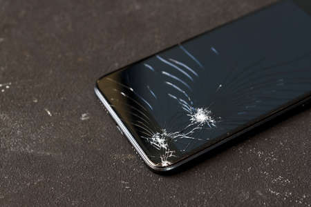 Broken glass of black smart phone on the dark background. Selective focus.