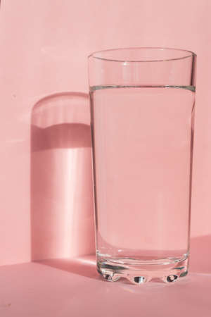 Close up of sparkling water in transparent high glass and sun glare on pink background.の写真素材