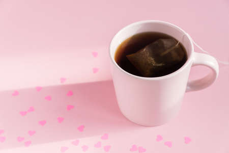 Pink cup with hot black tea on pink background with scattered paper hearts. Love and care concept. Copy space for text.の写真素材