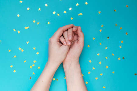 Female hands with nude manicure on blue background with scattered gold stars. Festive background. Concept of naturalnessの写真素材