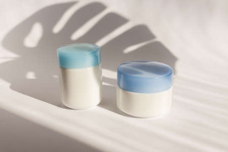 White blank mockup of bottle cream containers with blue cups. Monstera shadows. Professional tubes...