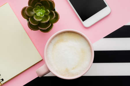 Top view of workspace with smartphone, cup of coffee and copy space on pink background.