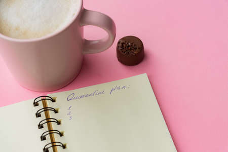 Self isolation concept. Open notepad with quarantine plan during coronavirus pandemia. Pink cup of capuccino with chocolateの写真素材