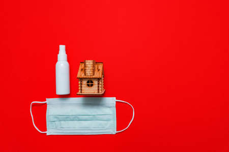 wooden house, sanitizer spray and protective medical face mask on red background as a symbol of behavior in quarantine during the coronavirus pandemicの写真素材