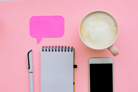 feminini desk workspace with smartphone, blank notepad, pen, cup of coffee on pink background. flat lay, top viewの写真素材