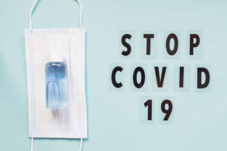 medical mask and sanitizer on blue background and text stop covid 19. hygienic quarantine concept. Flat lay, top view.の写真素材