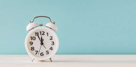 White alarm clock standing on wooden shelf on blue background. Banner with copy space fro your text...