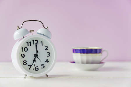 morning wake up. White alarm clock and cup of tea or coffee on white table with copy spaceの写真素材