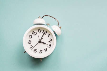 Flat lay white beautiful new alarm clock on blue color background. with copy spaceの写真素材