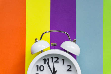 white alarm clock on multicolored striped background with copy space for text