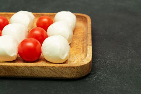 ripe tomatoes and mozzarella balls on wooden plate - Italian food ingredients with copy space