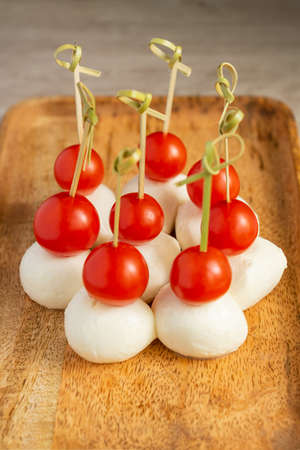 Food snacks and appetizers for buffet. Canapes with mozzarella cheese and cherry tomatoes served on wooden tray.の写真素材