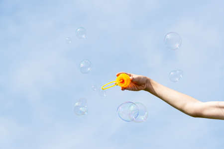 childs hand holding a wand for blowing soap bubbles against the blue sky on a sunny summer dayの写真素材