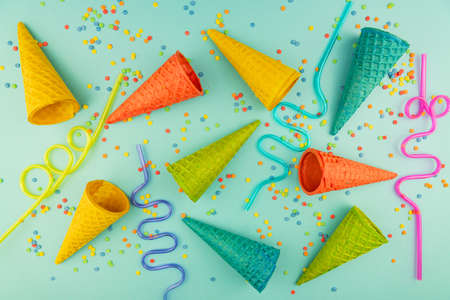 bright multicolored ice-cream waffle cones and cocktail straws on blue background with scattered...