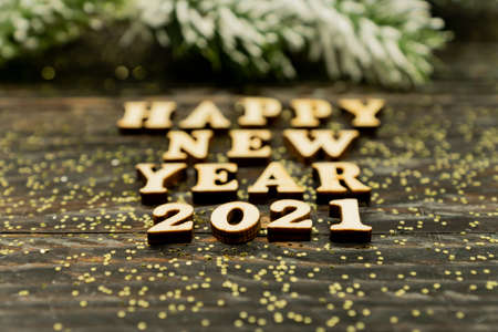Happy New year 2021 celebration. Wooden text and numbers 2021 on wooden background with scattered golden confetti and fur tree branch.の写真素材