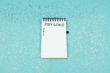 Small notebook on blue confetti background with written 2021 goals for new year. Resolutions list