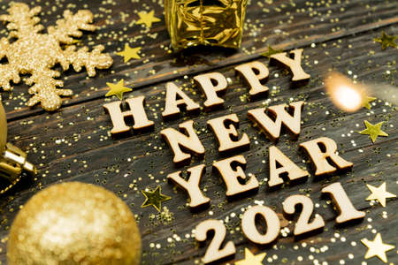 Happy new year 2021 text on wooden background surrounded golden christmas toys and fur tree branch. Festive greeting catd for holidays.の写真素材