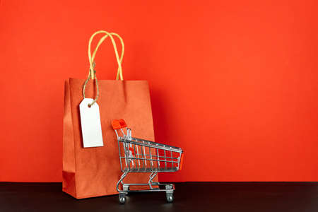 Shopping lover concept: Red paper shopping bags and small toy shopping cart on red backgroundの写真素材