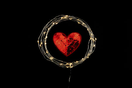 Red Heart in the circle of holiday celebration light garland on black background. Romantic...