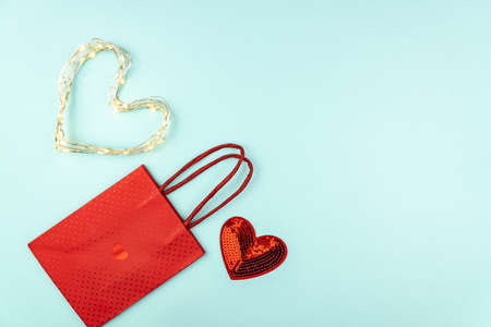 Valentines day creative concept. Red sequins heart, paper bag and heart shape led garand on blue background. Top view, flat lay, copy space for text. Holiday celebration tempate.の写真素材